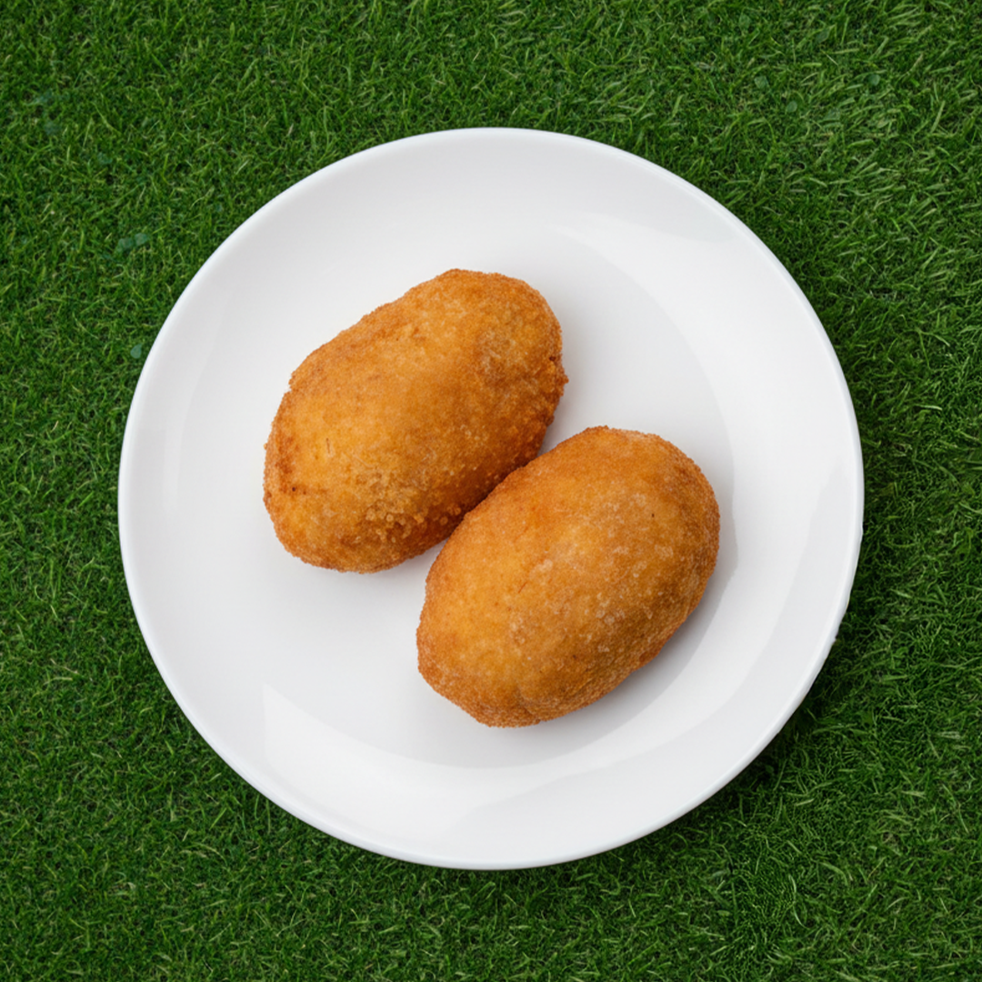 Due crocchette di patate dorate su un piatto bianco posato sull'erba verde.