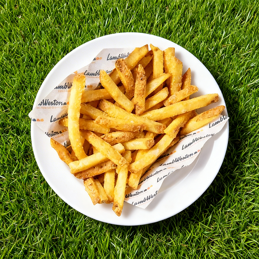 Piattino bianco con patatine fritte croccanti su carta da forno, posato su prato verde.