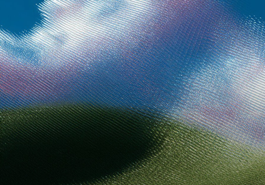 An abstract image with a heavy, linear glass-like distortion over what appears to be a landscape. Fine horizontal ridges create a shimmering effect across colors of deep blue, soft pink, and vibrant green. The texture mimics the look of looking through ribbed privacy glass at a sky and grassy field.