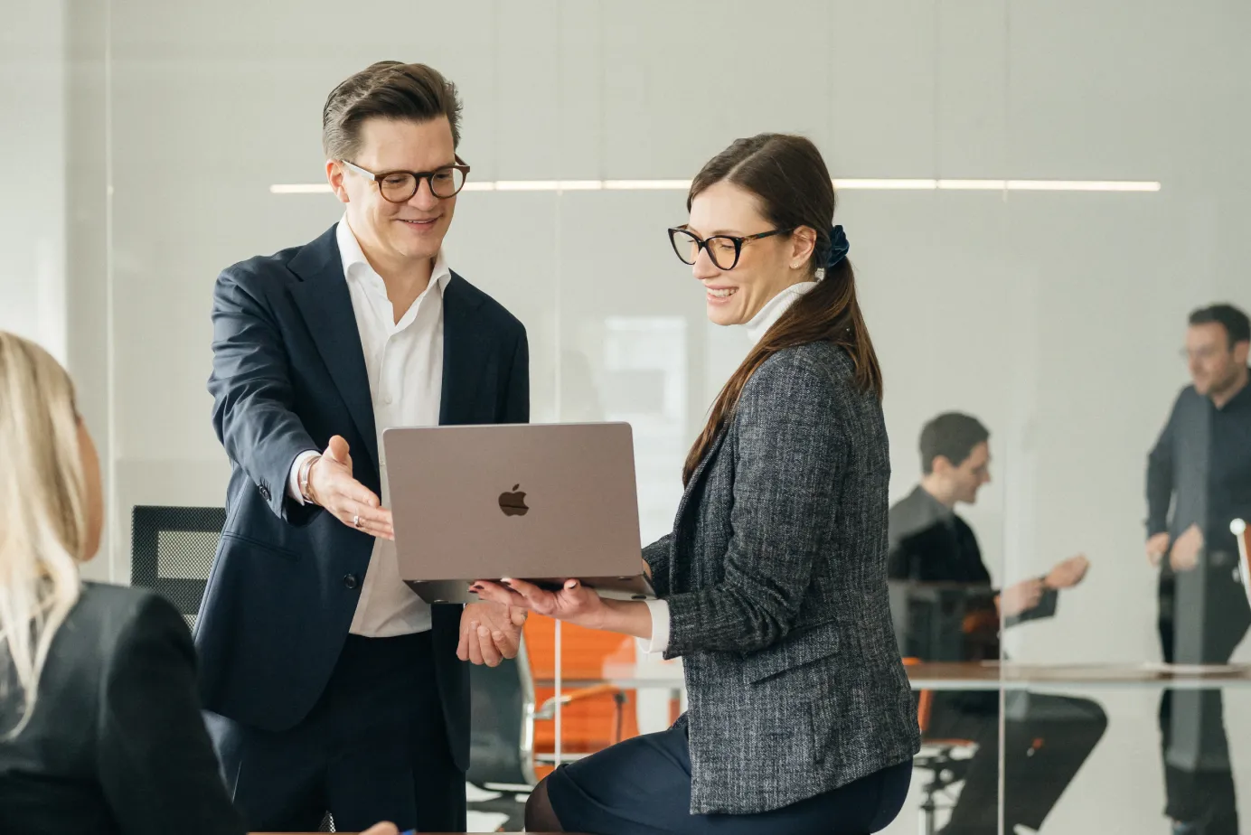 Zwei Geschäftsleute in Brillen schauen lächelnd auf einen Laptop in einem modernen Büro.