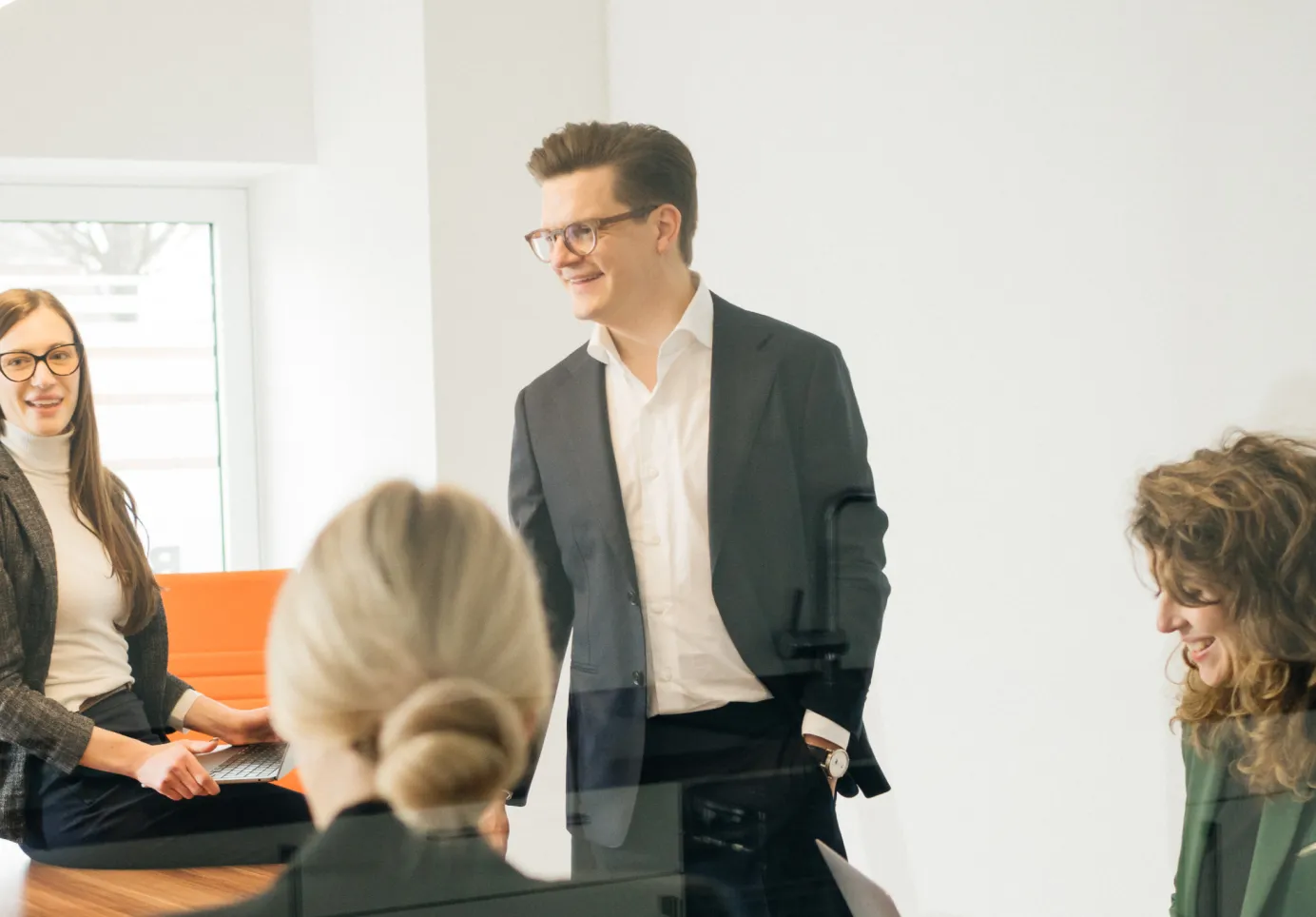 Vier Berufstätige, die in einem hellen Büro in einem entspannten Meeting lächeln und sprechen.