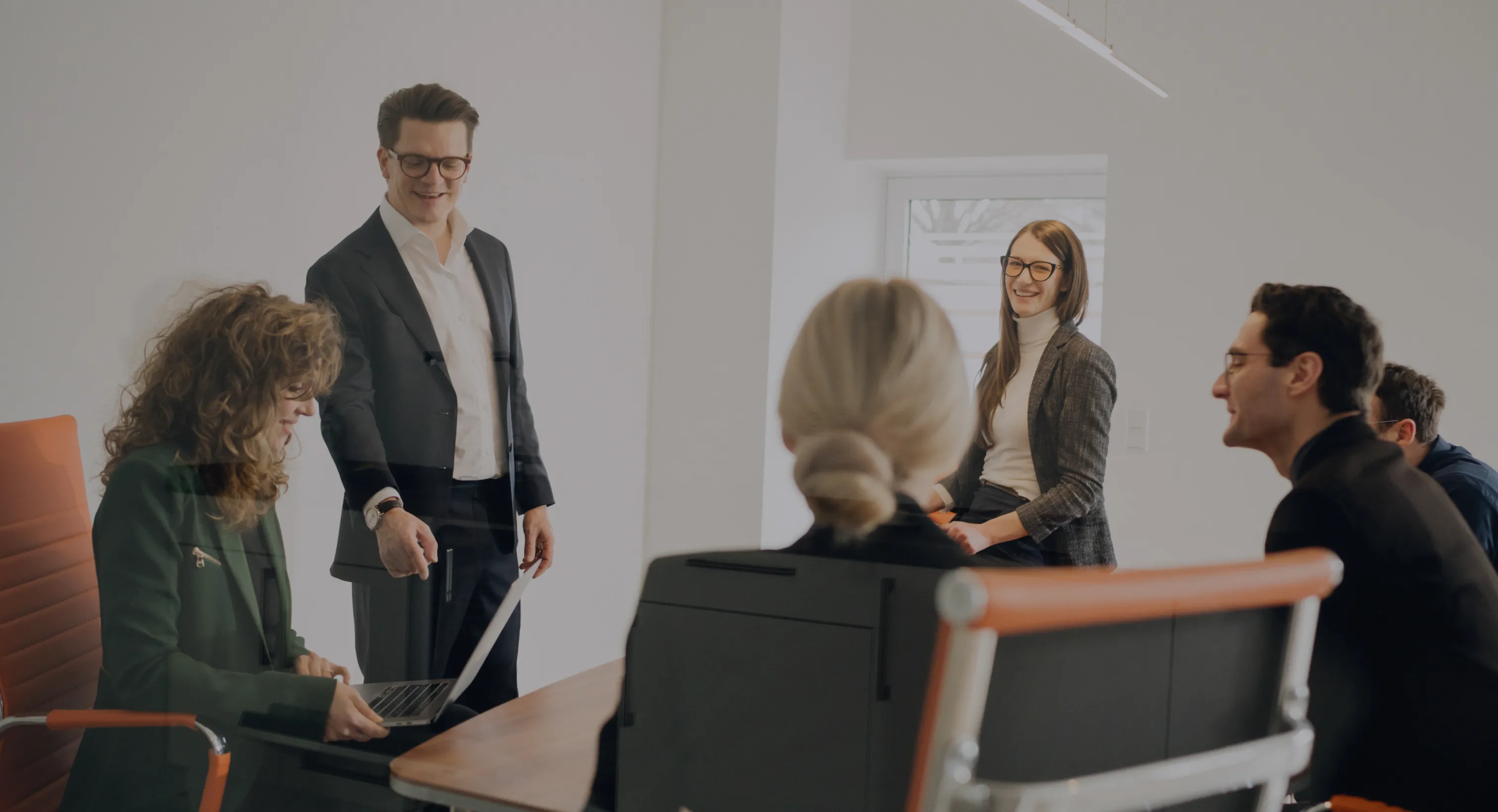 Gruppengespräch in einem modernen Büro mit fünf Personen, die an einem Besprechungstisch sitzen und stehen.