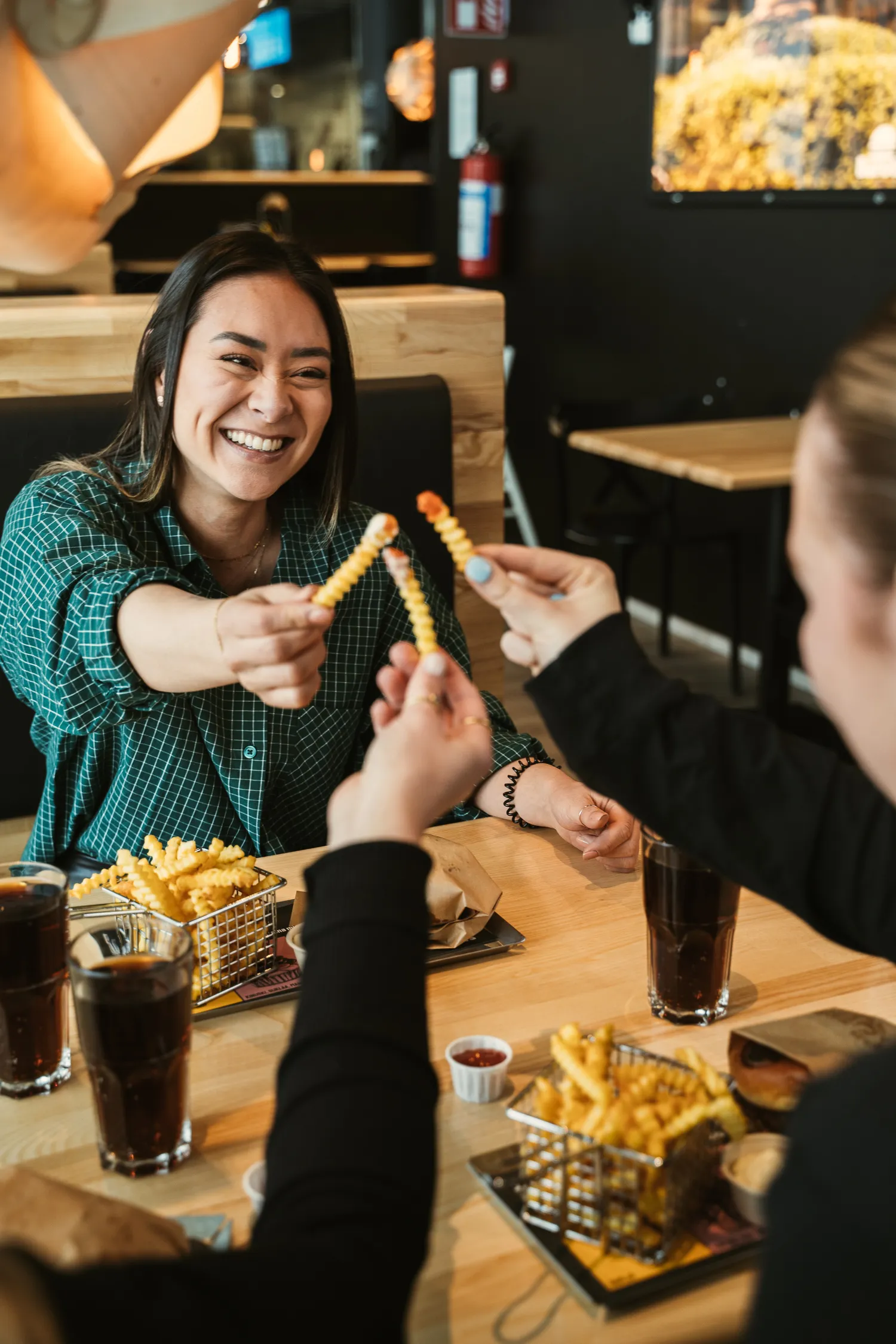 Kaksi miestä istuu ravintolapöydän ääressä, hymyilee ja kohottaa voileipiä kilistääkseen, pöydällä on ruokaa ja juomia.