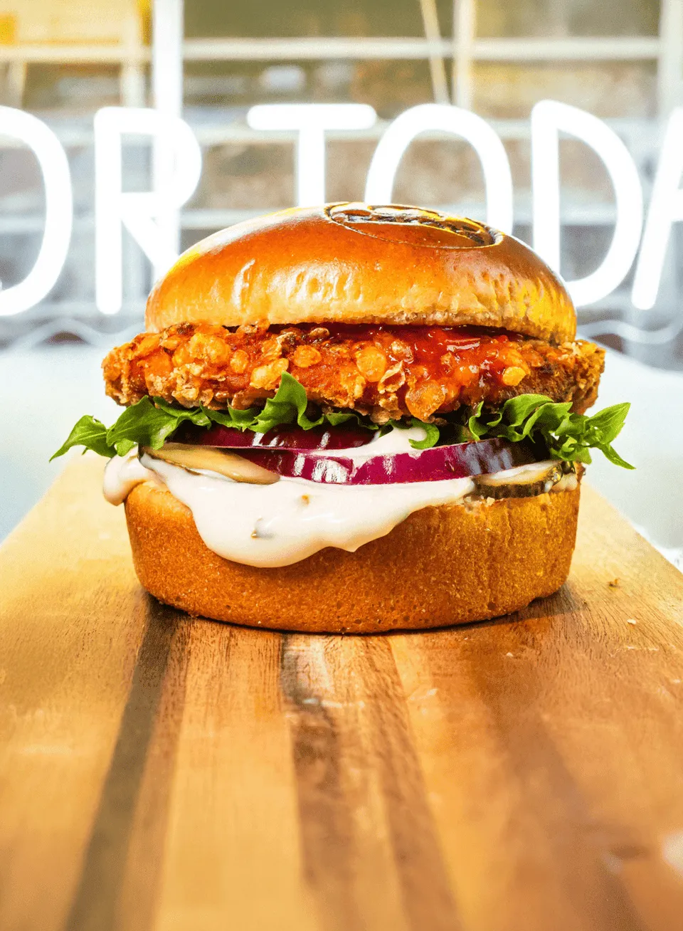 Rapeaksi paistettu kanaleipä, jossa on salaattia, viipaloitua punasipulia, suolakurkkua ja kermaista kastiketta paahdetussa sämpylässä.