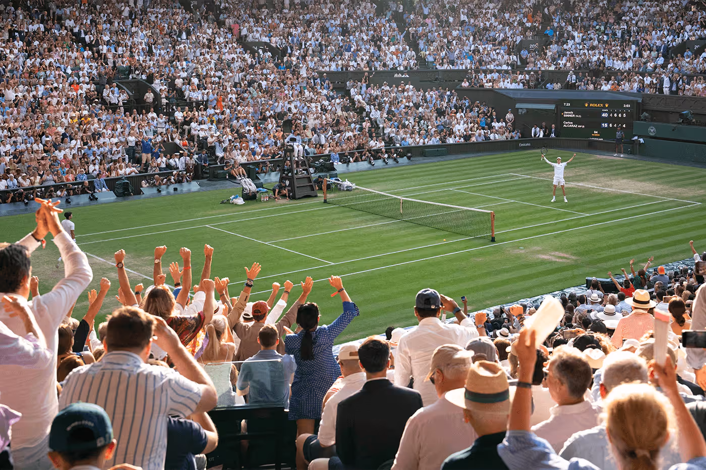 Crowd cheering in a packed stadium as a tennis player celebrates victory on a grass court at Wimbledon.