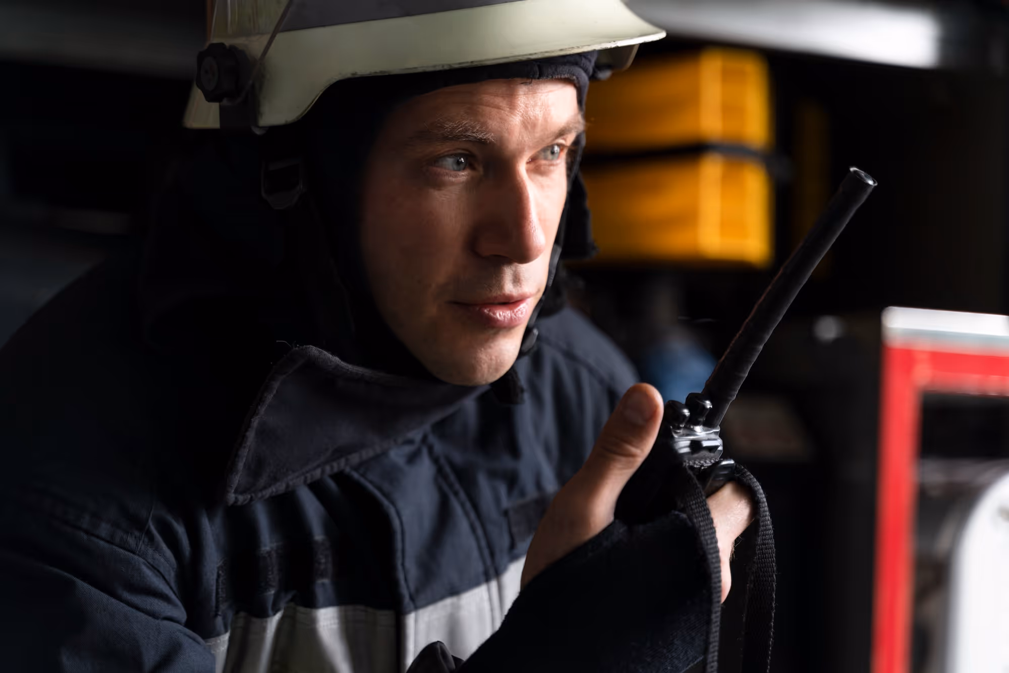 Firefighter in protective helmet and uniform speaking into a handheld radio.