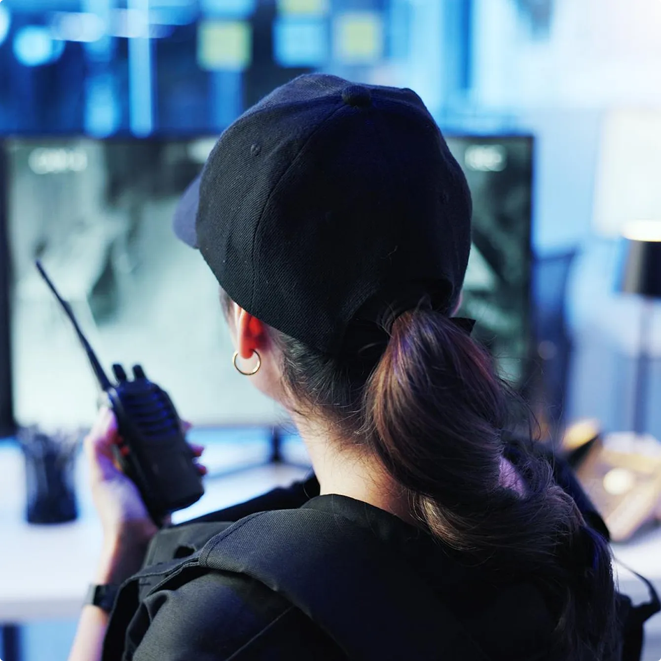 Security personnel holding a walkie-talkie and monitoring surveillance screens.