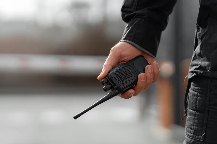Person holding a black walkie-talkie with a long antenna in their hand.