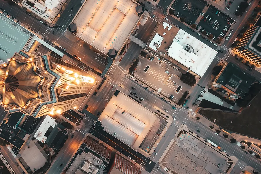Aerial view of an urban intersection surrounded by illuminated buildings and parking lots at dusk.