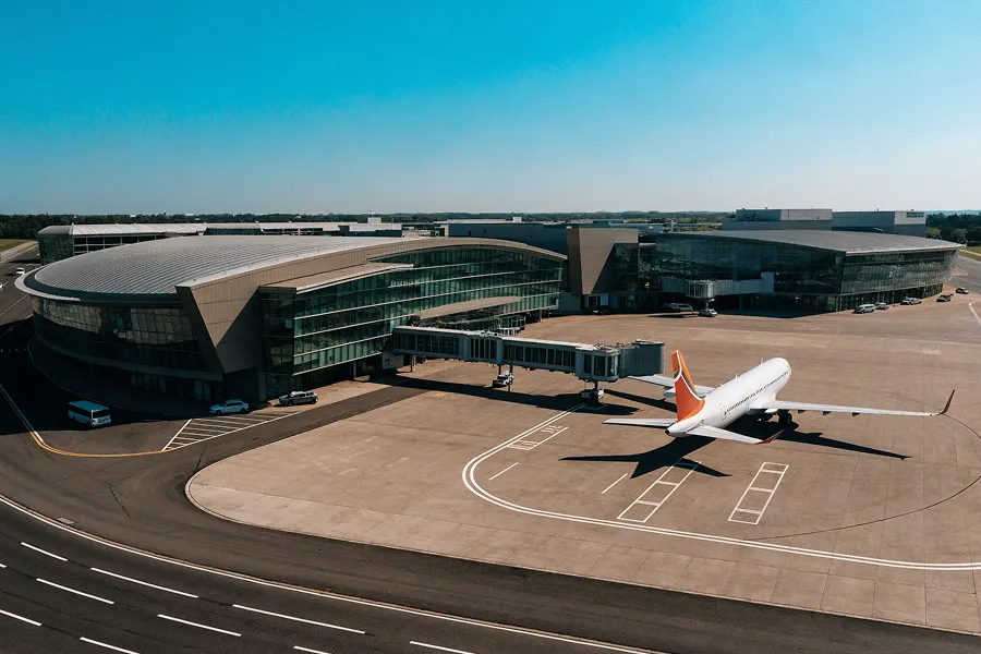 Commercial airplane parked at a modern airport terminal with aerobridge connected on a sunny day.