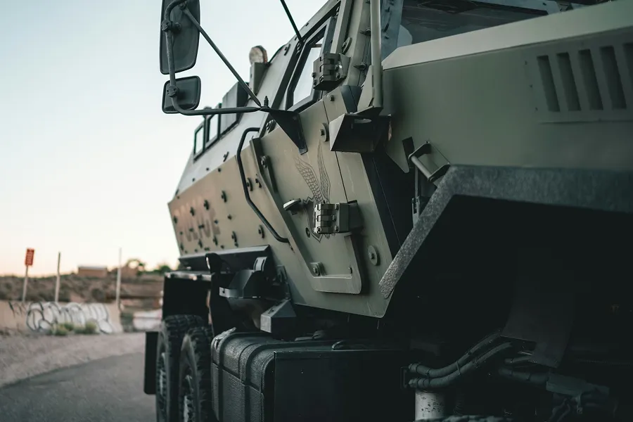 Close-up of an olive drab military armored vehicle parked on a road at dusk.