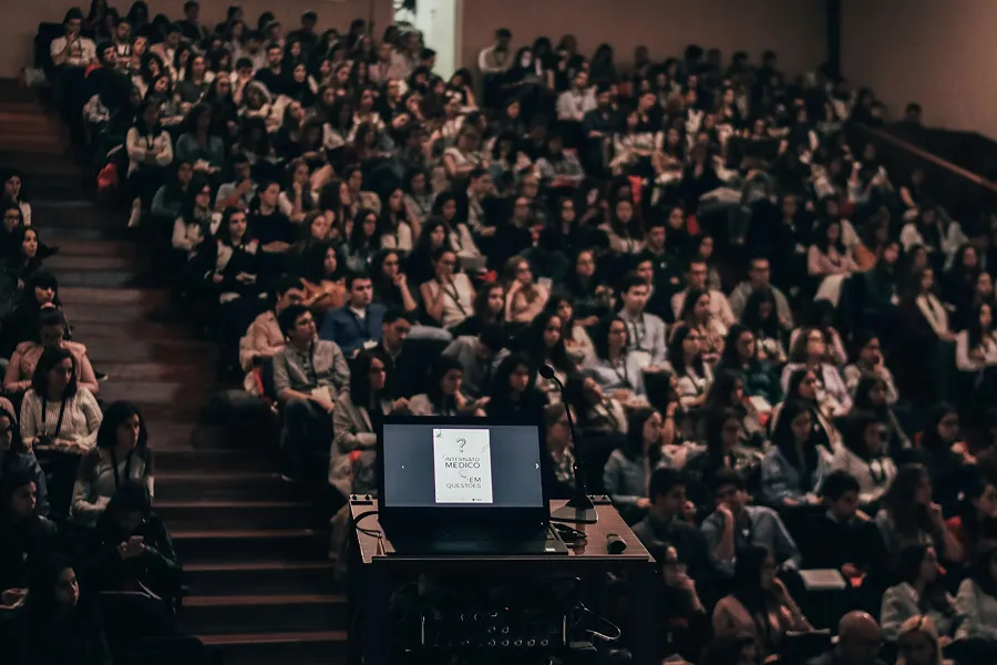 Lecture hall filled with an audience sitting and listening, seen from behind a podium with a laptop and microphone.