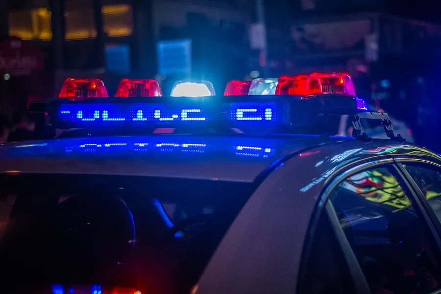 Close-up of police car roof with flashing red and blue emergency lights illuminating a city street at night.