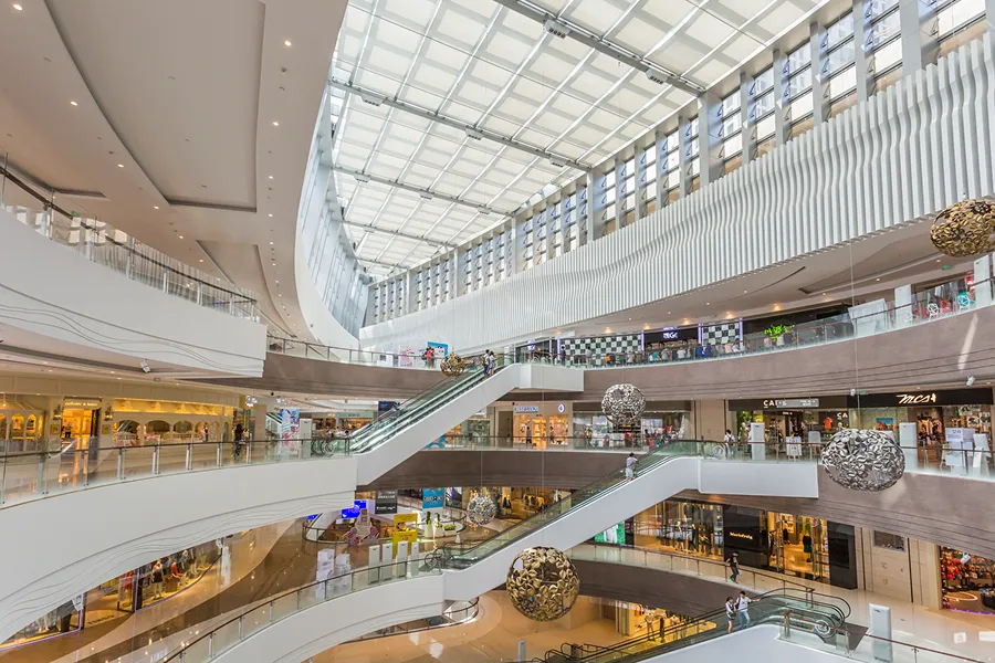 Multi-level modern shopping mall interior with escalators and decorative spherical hanging ornaments.