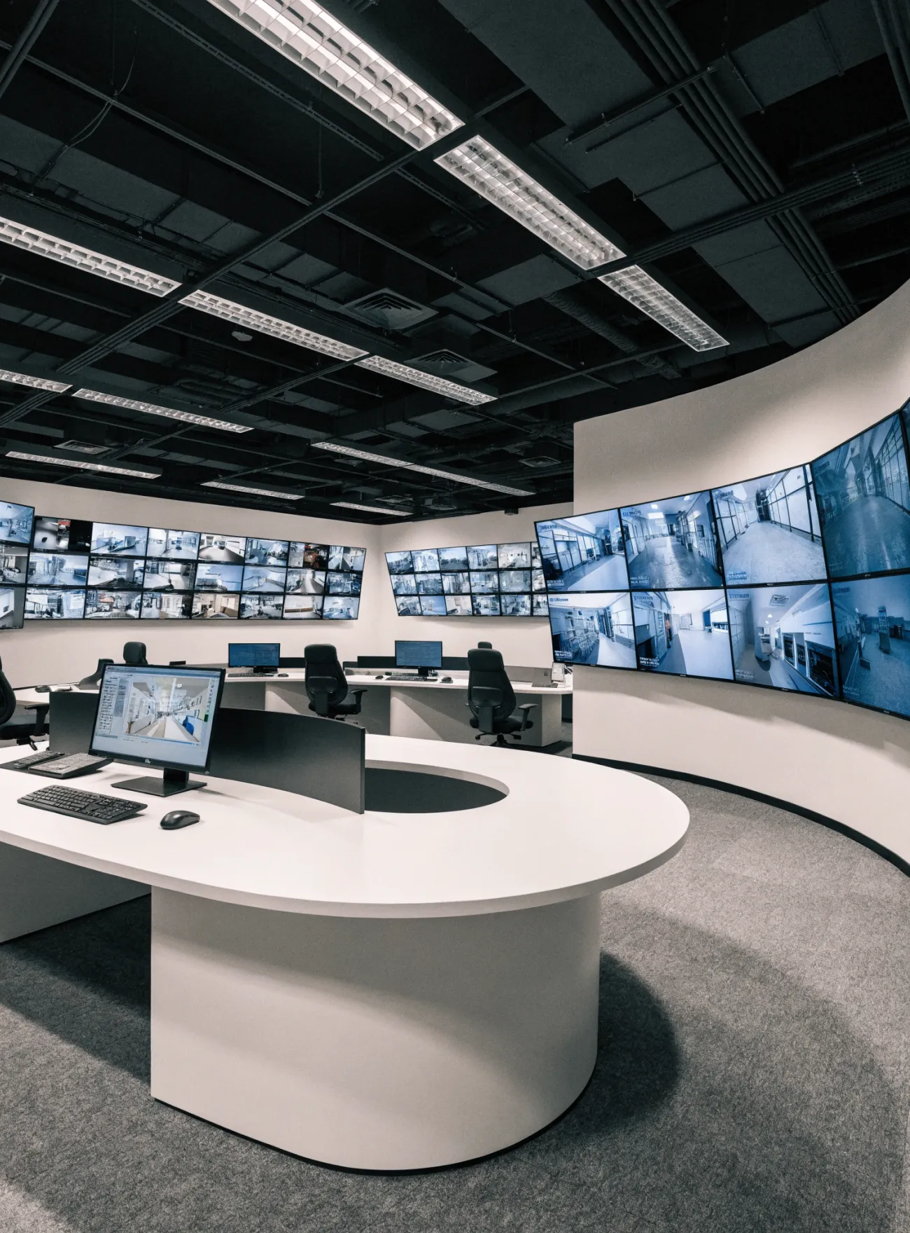 Modern control room with multiple screens showing security camera footage on curved walls.