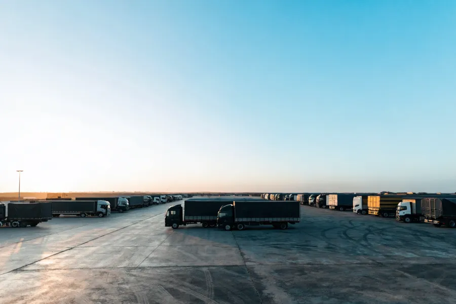 Large parking lot with rows of black and white trucks lined up under a clear blue sky at sunrise.