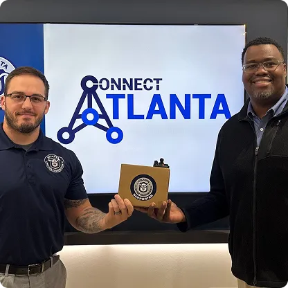 Two men smiling and holding a small wooden plaque in front of a screen displaying the Connect Atlanta logo.