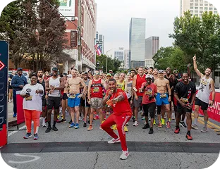 Crowd of runners at the start line of a city marathon event with buildings in the background and a man in red leading.