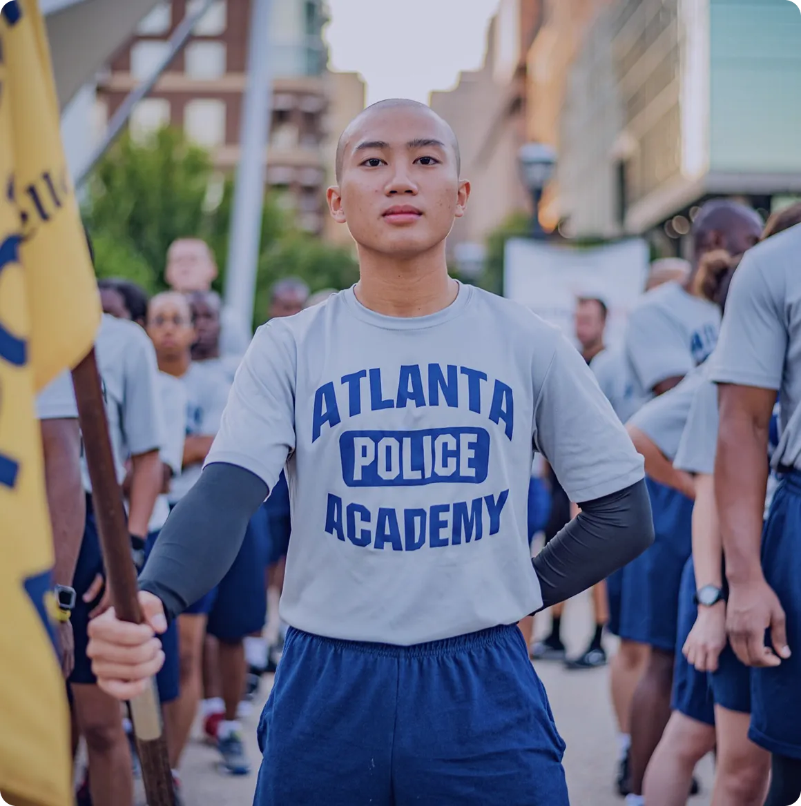 Young person standing confidently holding a yellow flag, wearing an Atlanta Police Academy t-shirt during an outdoor group event.