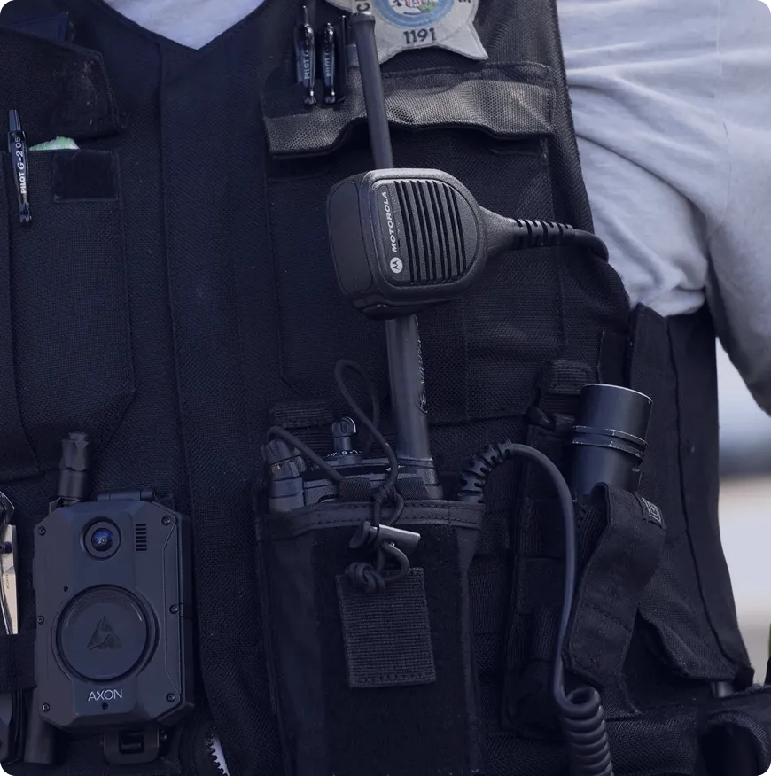Close-up of a police officer's tactical vest equipped with a Motorola radio microphone and an Axon body camera.