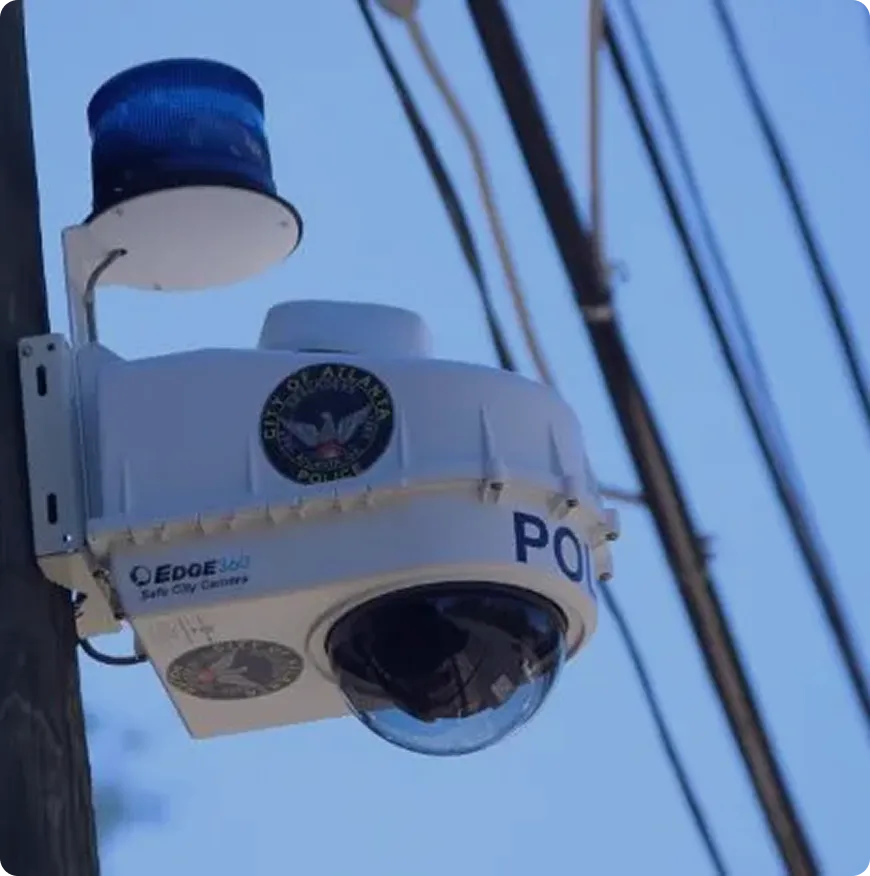 Police surveillance camera with blue light mounted on a pole against a blue sky background.