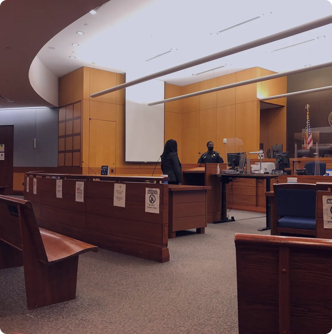 Empty courtroom with wooden benches, a security officer behind the desk, and a person standing in front of the officer.