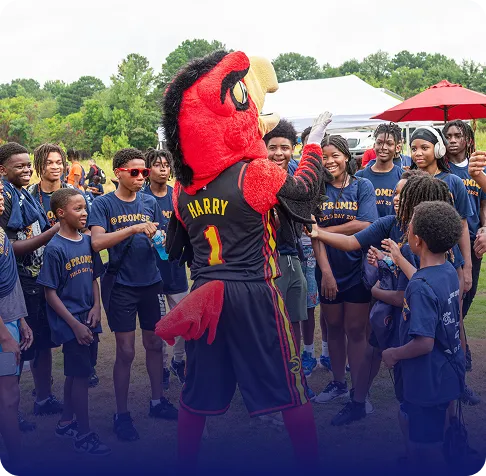 Group of smiling children in blue t-shirts gathered outdoors around a red bird mascot named Harry.