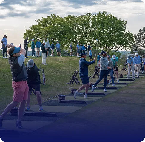 Group of people practicing golf swings at a driving range outdoors under a cloudy sky.