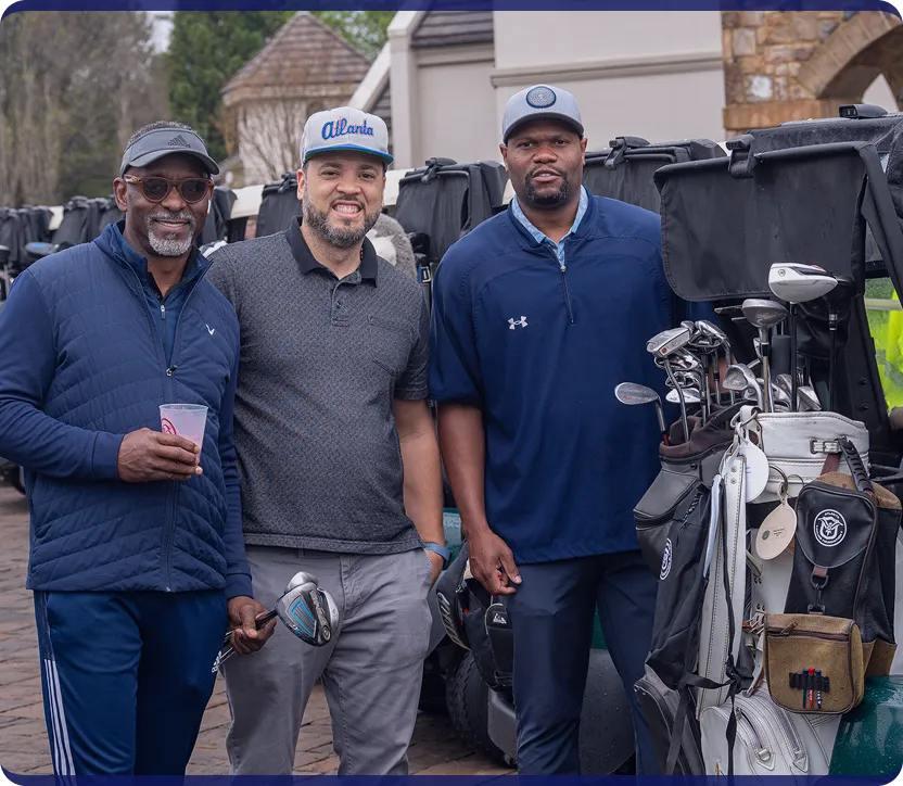 Three men standing together smiling near golf carts and golf bags filled with clubs.