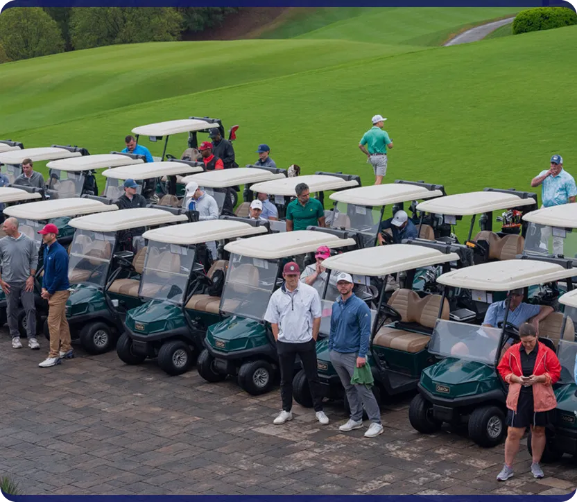 Group of people standing and sitting near a row of green golf carts with beige roofs on a golf course.