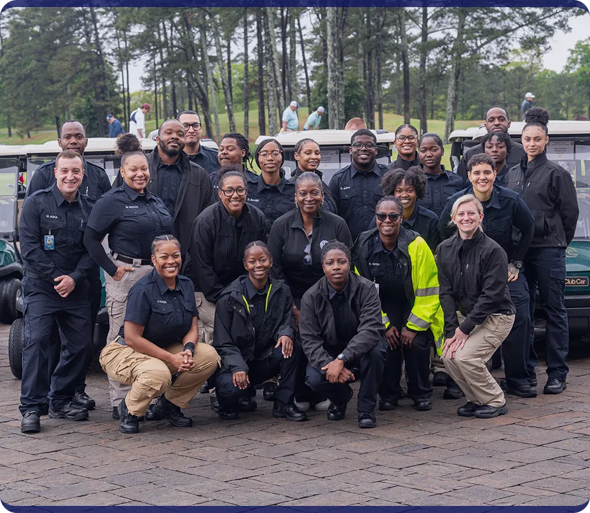 Group portrait of diverse smiling security or law enforcement team posing outdoors in front of golf carts and trees.