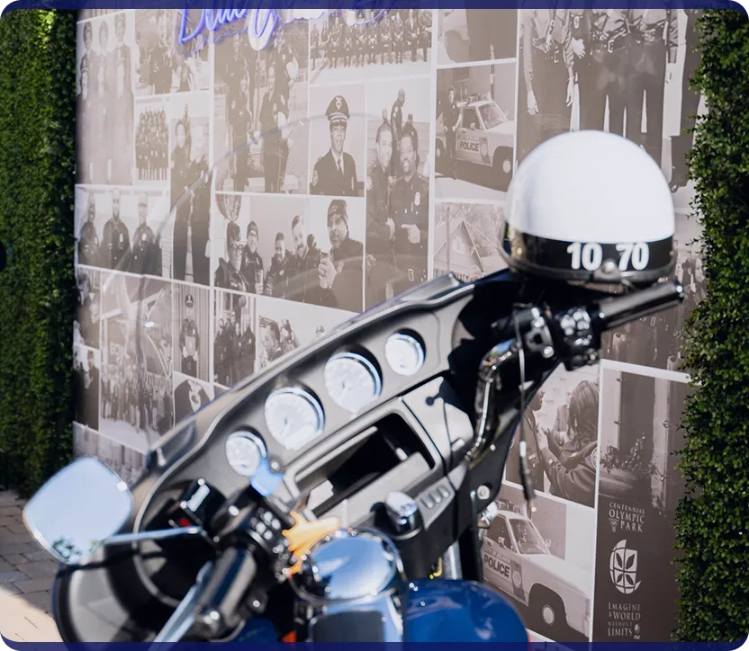 Police motorcycle with helmet marked 10 70 parked in front of a collage wall of black and white police photos.
