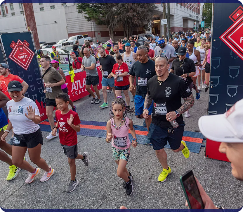 Diverse group of runners, including children and adults, starting a road race at Atlanta's Finest 5K event.