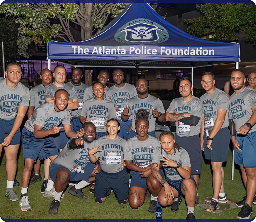 Group of diverse Atlanta Police Academy cadets posing together in front of a tent labeled The Atlanta Police Foundation at night.