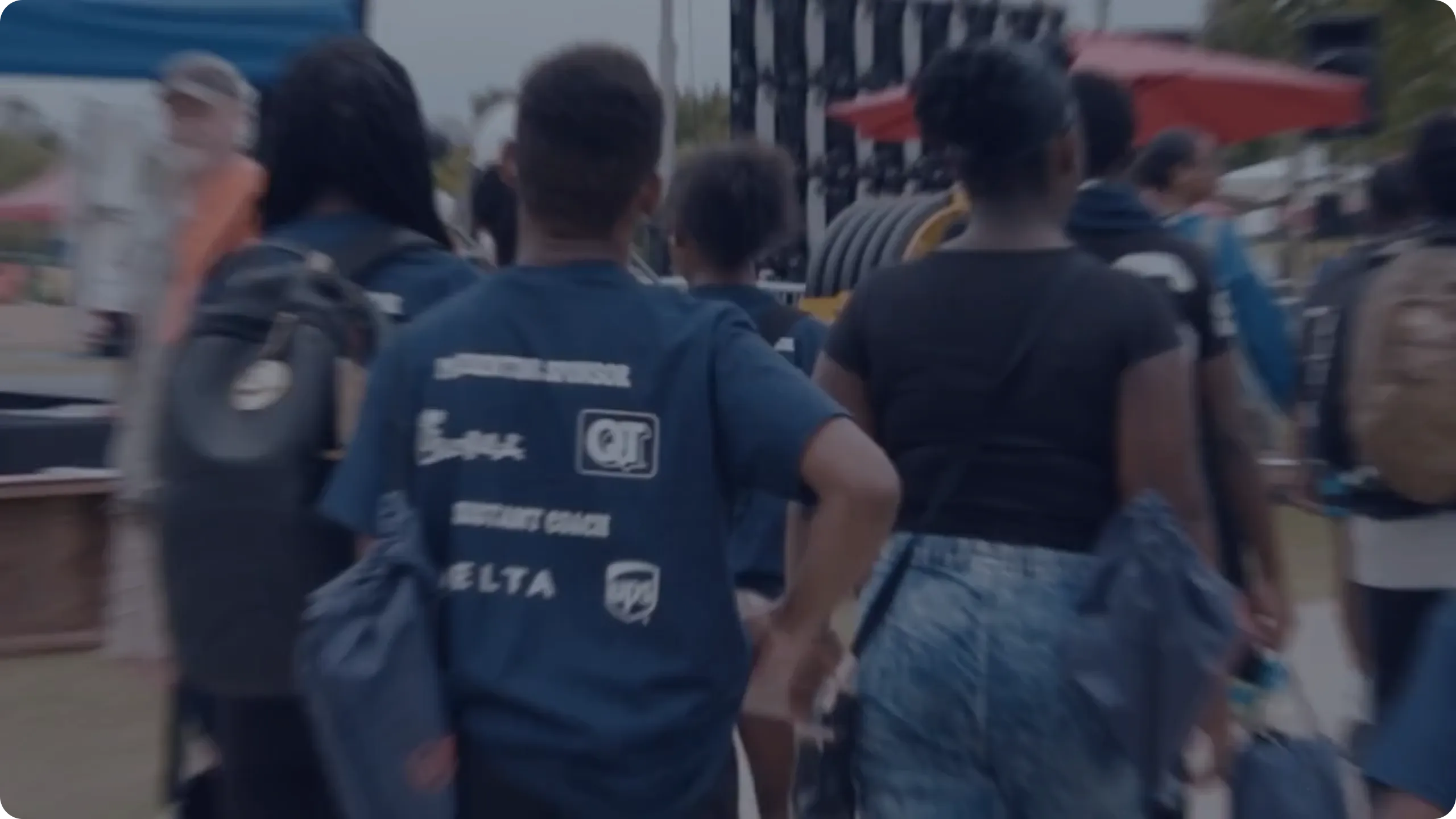 Group of people walking outdoors, some wearing blue shirts with logos and carrying bags.