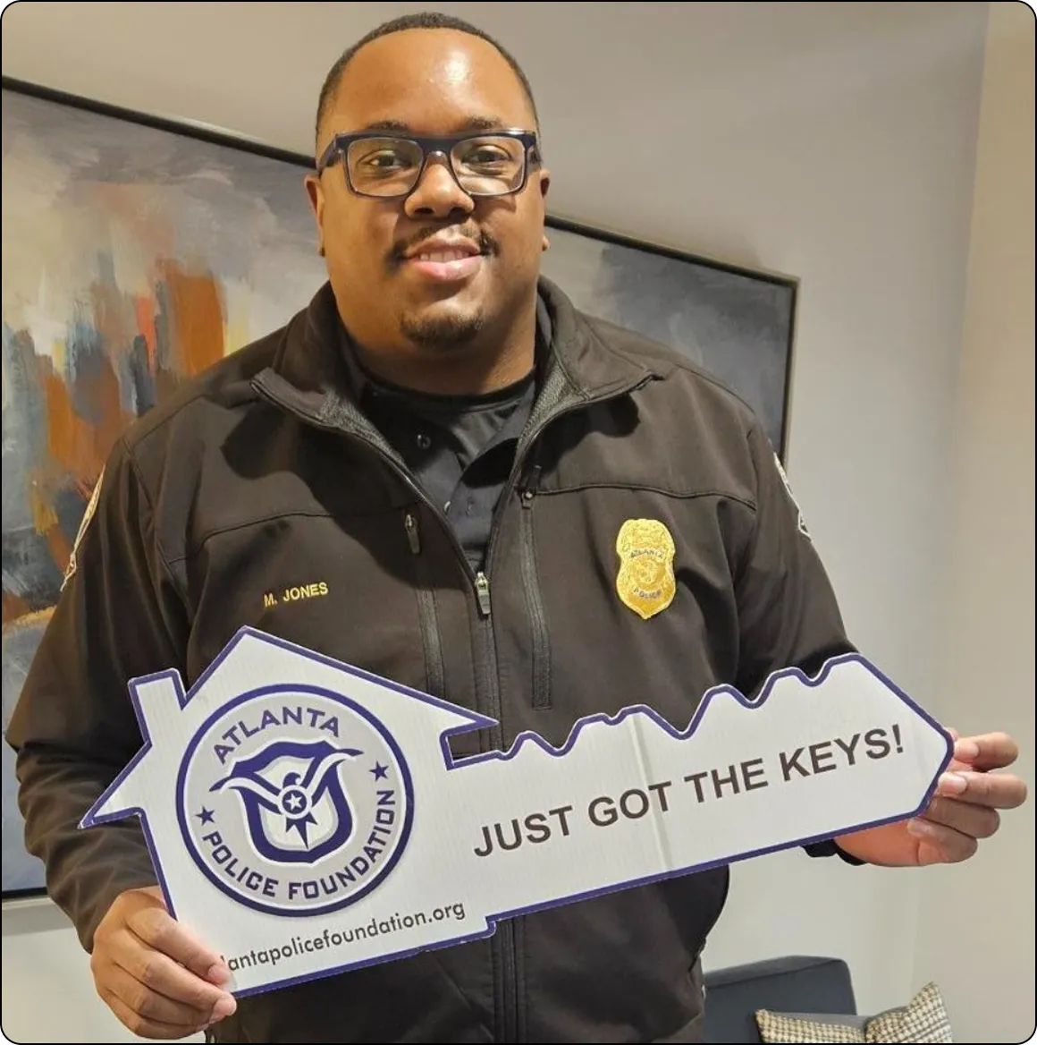 Man in police uniform holding a large key-shaped sign that reads 'ATLANTA POLICE FOUNDATION JUST GOT THE KEYS!'