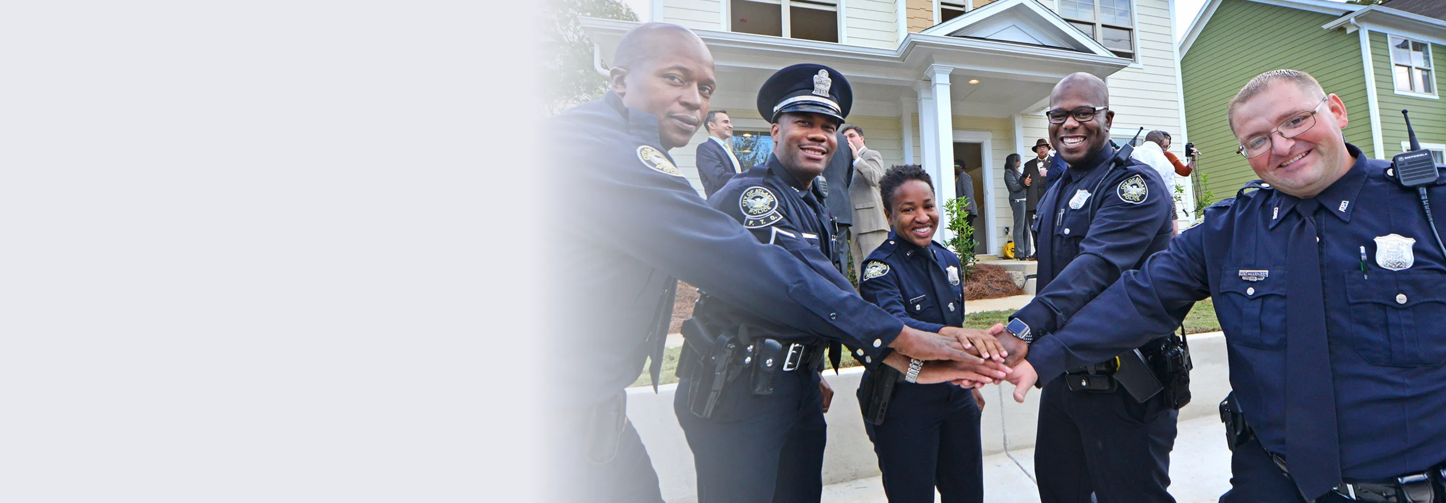 Five police officers standing outside a house with their hands stacked together in unity.