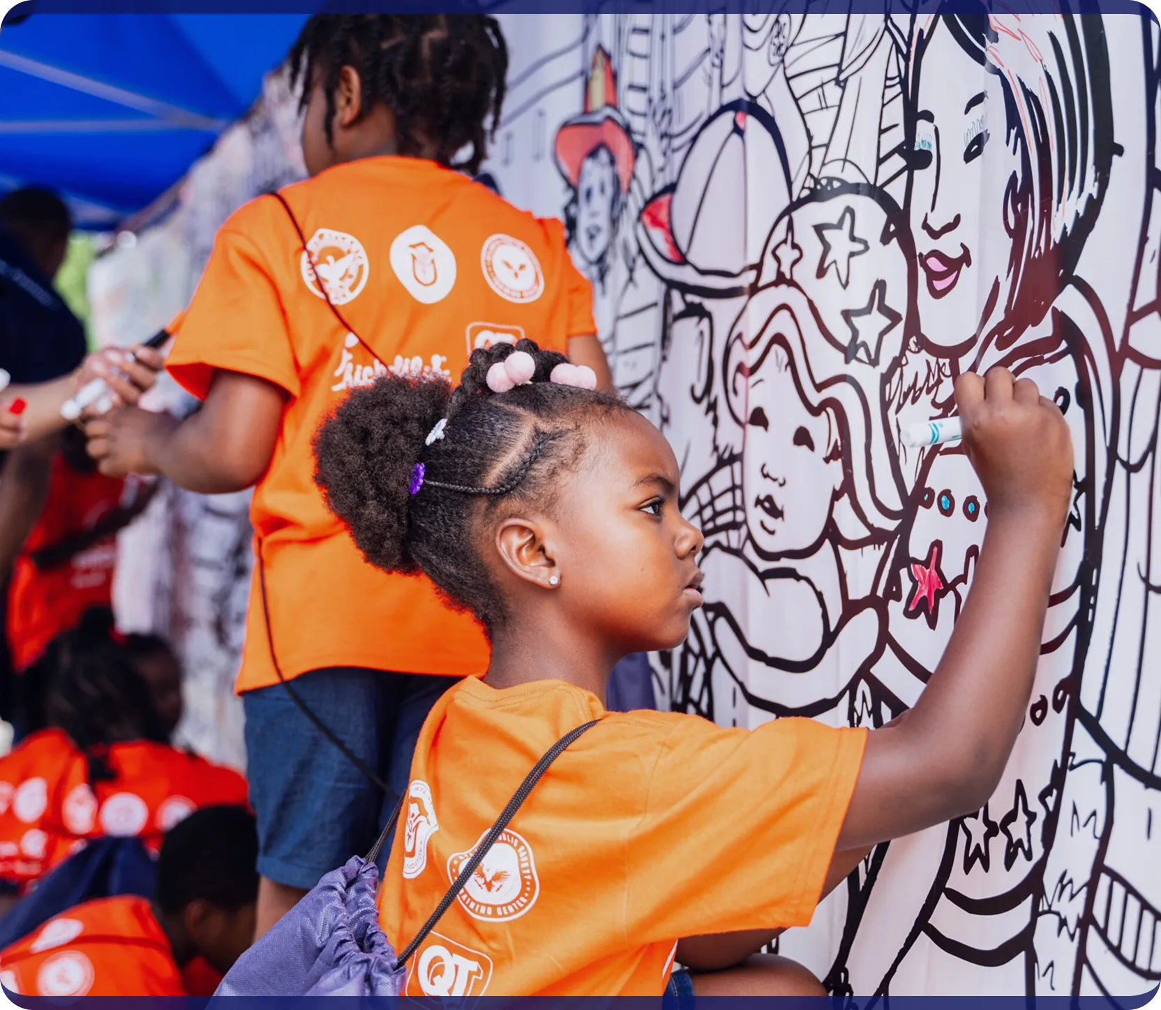 Young girl in an orange shirt coloring a large black-and-white mural featuring various cartoon characters.
