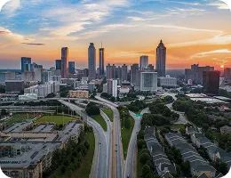 Sunset view of a city skyline with highways curving through urban and residential areas.