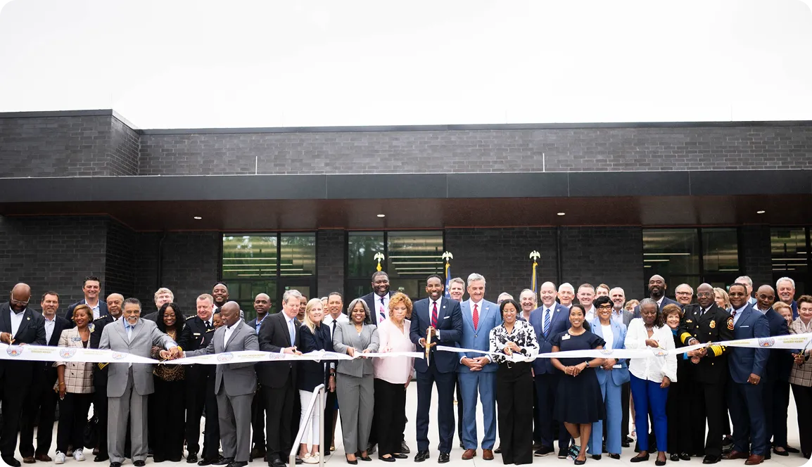 A diverse group of people in business attire standing in front of a modern building, participating in a ribbon-cutting ceremony.