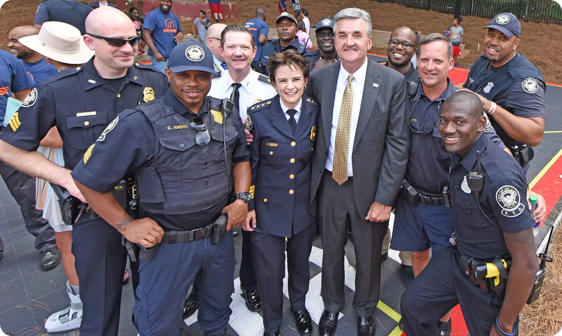 Group of police officers and a man in a suit posing together outdoors and smiling.
