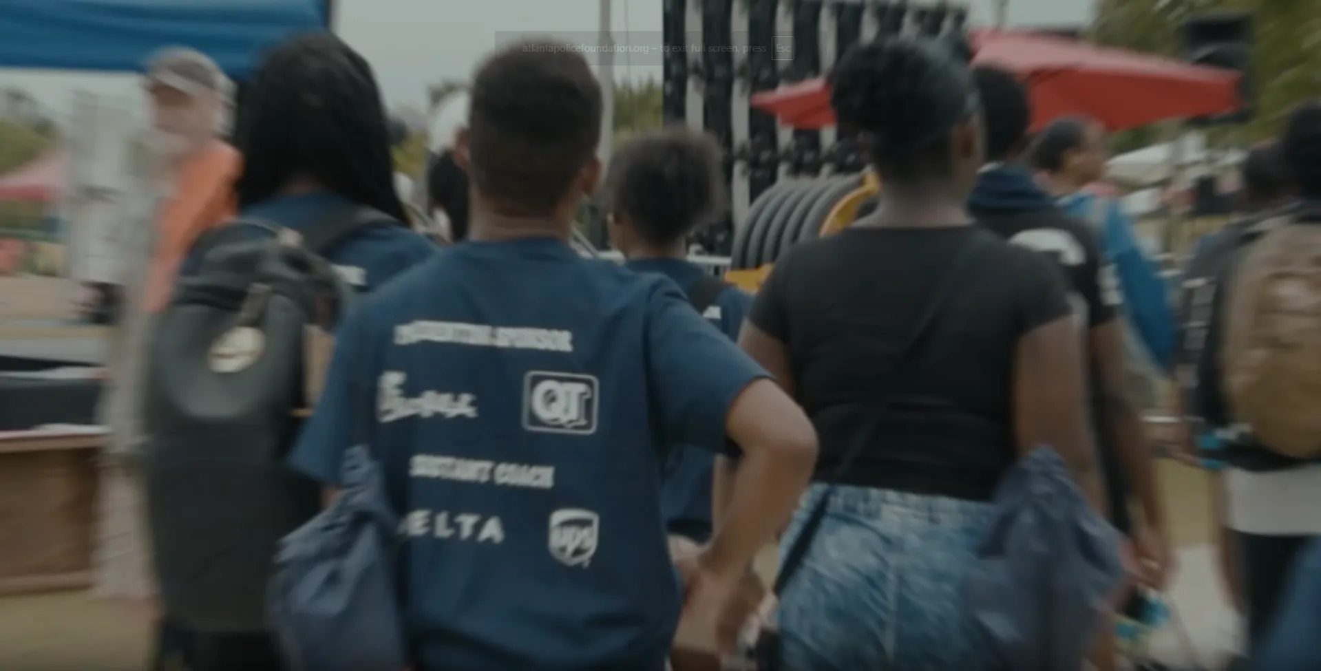 Group of young people walking outdoors at an event with promotional t-shirts and backpacks.