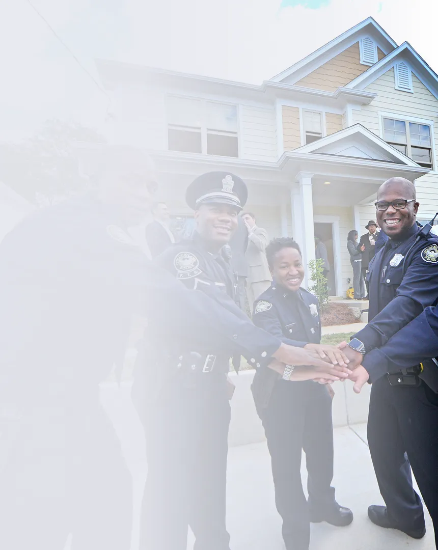 Group of smiling police officers standing outside a house with their hands joined in teamwork.