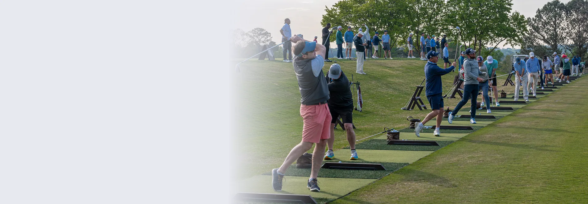 Multiple golfers practicing their swings on a driving range with a grassy area and trees in the background.