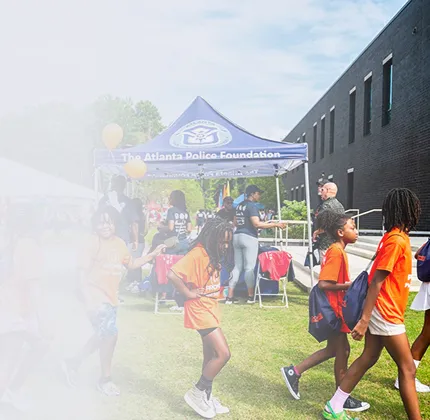 Children in orange shirts walking and playing near a blue tent with The Atlanta Police Foundation logo at an outdoor event.