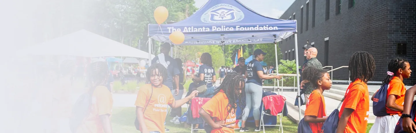 Children in orange shirts at an outdoor event with a blue tent labeled The Atlanta Police Foundation.