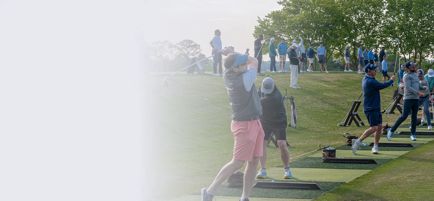 Multiple people practicing golf swings at a driving range with green grass and trees in the background.