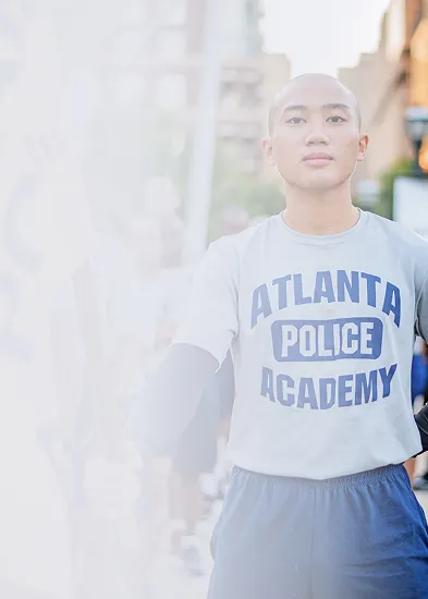 Young man wearing an Atlanta Police Academy t-shirt standing with an outstretched arm on a city street.