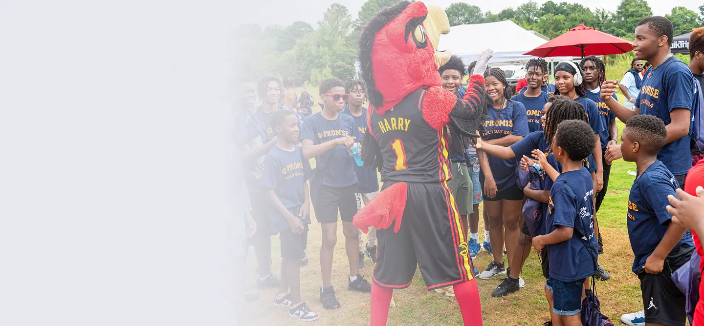 Children and teenagers in matching 'Promise Field Day 2024' shirts interacting with Harry the Hawk mascot outdoors.