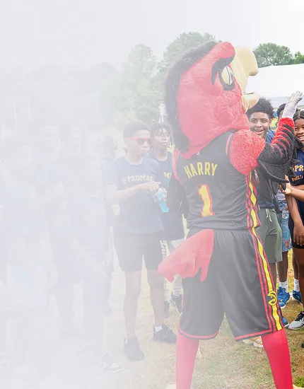 Mascot named Harry in a red bird costume interacting with a group of smiling children outdoors.